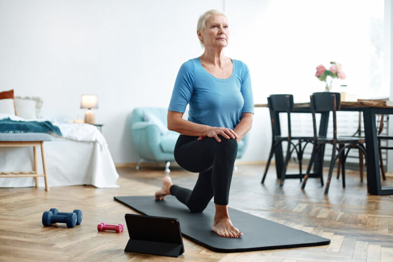 elderly woman doing exercises with an online trainer in her living room. concept of online training.